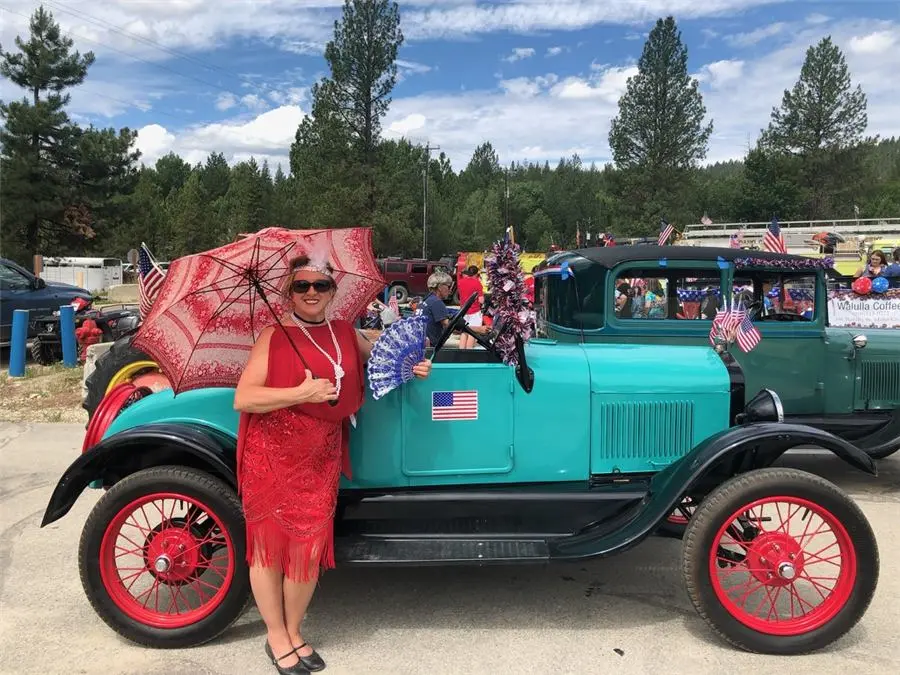 CarrieAnne in a red dress beside a teal classic car at a parade